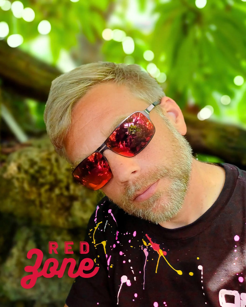 Ein Mann Anfang 40 sitzt mit seiner Edelstahlsonnenbrille und rot verspiegelten Brillengläsern, lässig in die Kamera. Er hat…